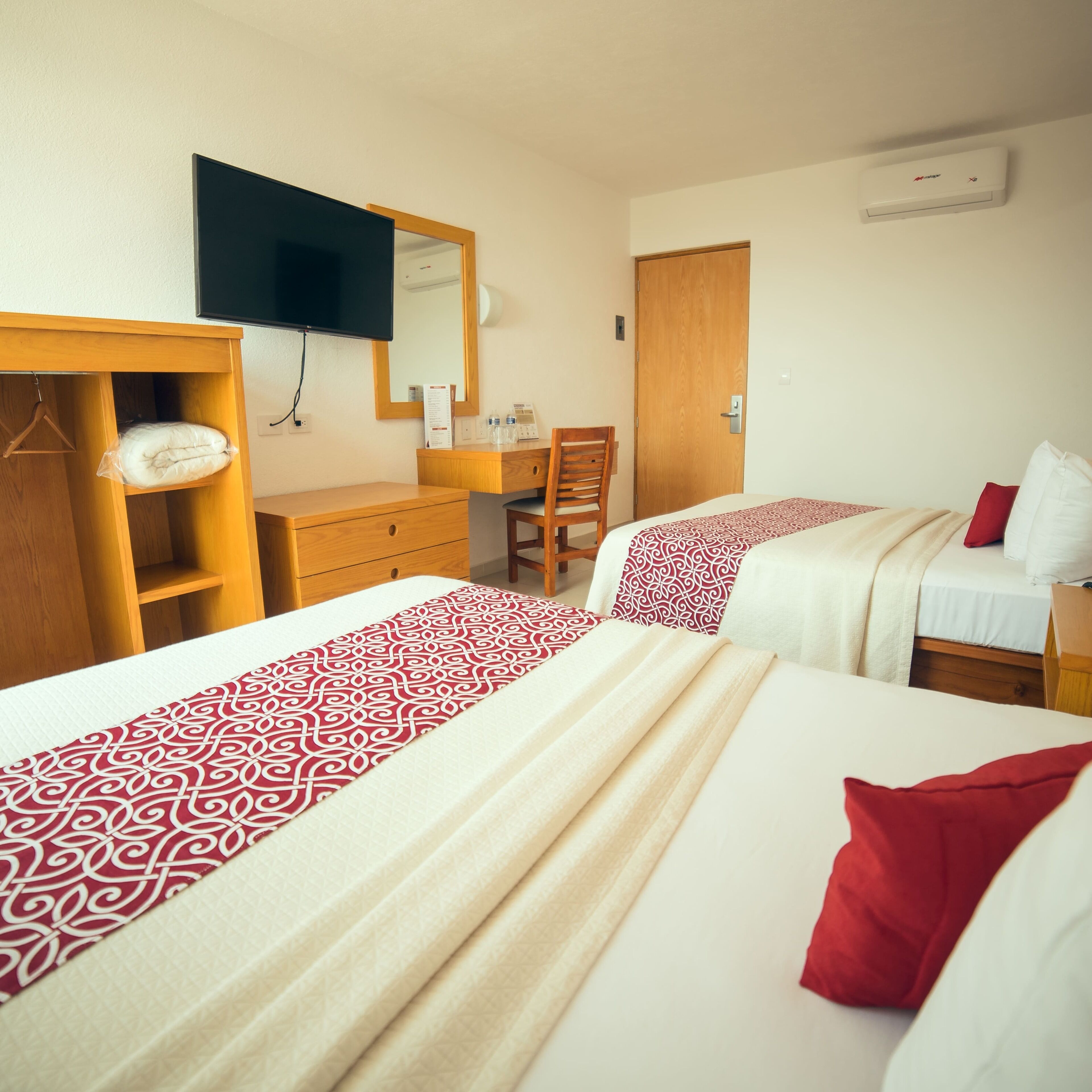 Habitación de hotel con dos camas, cómoda de madera, escritorio, silla, espejo y televisión.