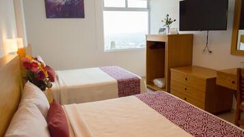 A hotel room with two beds, a wooden dresser, a TV, and a window with a city view.