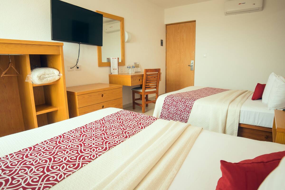 Ein Hotelzimmer mit zwei Betten, einem Holzschrank, einem Schreibtisch, einem Stuhl, einem Spiegel und einer Klimaanlage.