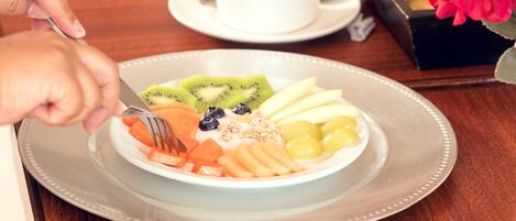 A breakfast setting with a plate of fruit, a cup of coffee, and a flower arrangement.