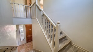 Un escalier avec une rampe et des balustrades blanches, menant à une porte en bois et à un palier situé au deuxième étage.