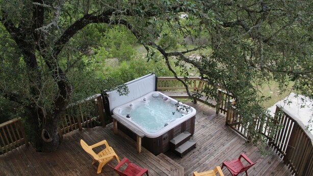 Un bain à remous sur une terrasse en bois, avec quatre chaises, entouré d’arbres.