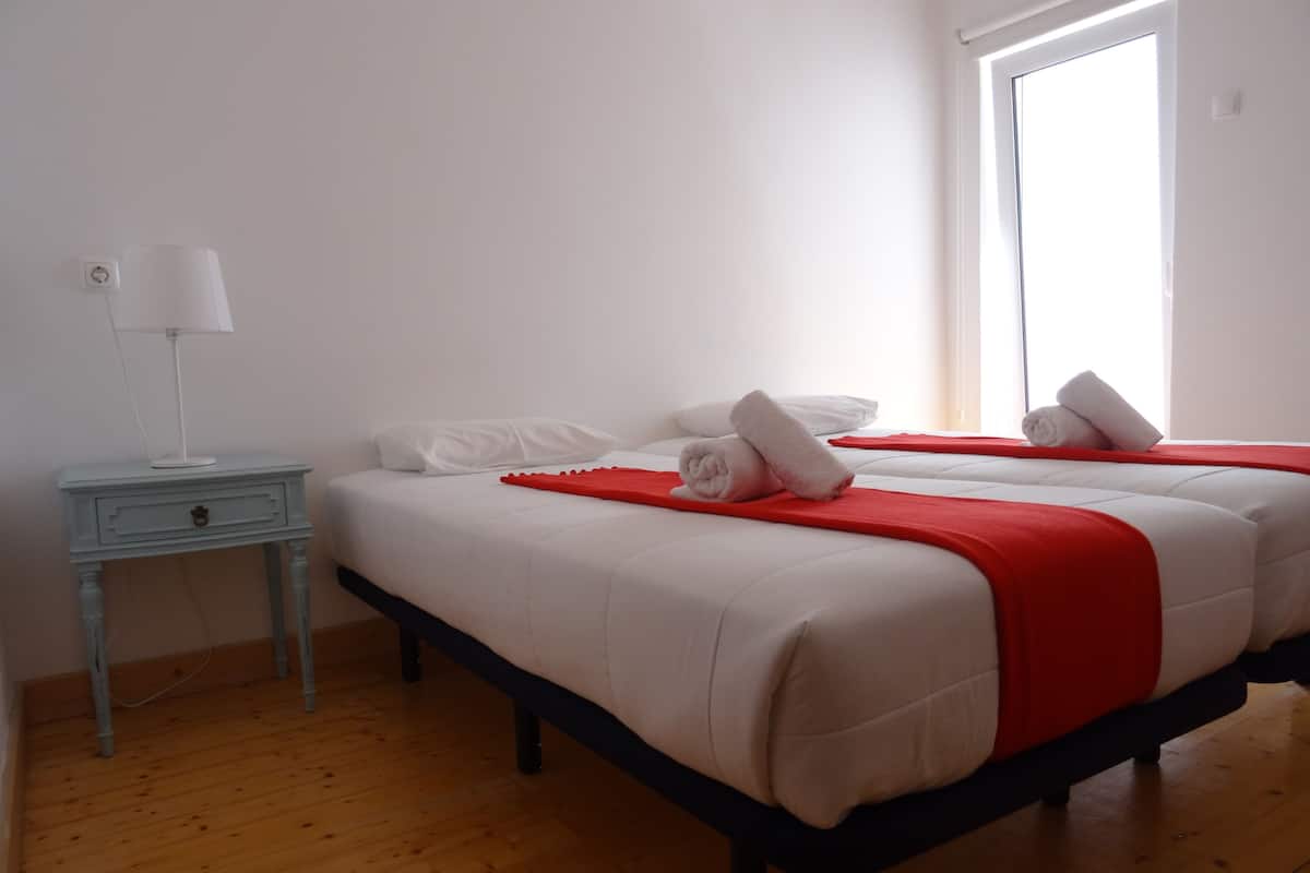 A bedroom with a double bed, a nightstand, a lamp, and a window.