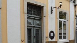 A building with a large grey door, a window with a sign, and a cobblestone street. - Guest House do Largo (Faro)