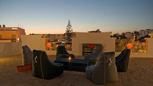 A rooftop terrace with modern outdoor seating, a fire pit, and a view of the cityscape at dusk. - Guest House do Largo (Faro)