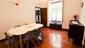A dining area with a round table, chairs, a clock, and a window with a view. - Guest House do Largo (Faro)