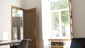 A room with a wooden floor, a desk, a chair, a window with a view of trees, and a ceiling light fixture. - Guest House do Largo (Faro)
