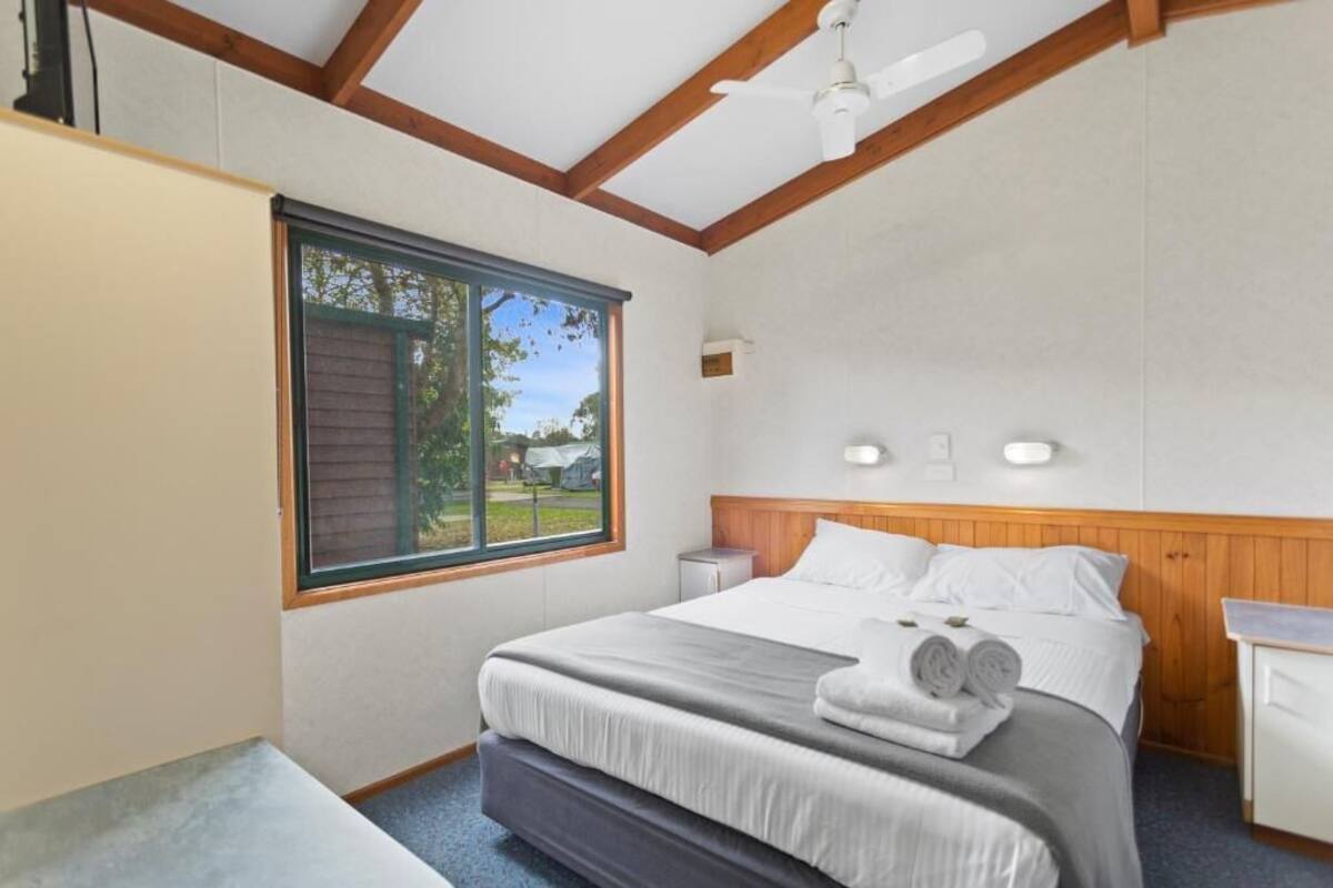 A bedroom with a bed, a window, a ceiling fan, and a bedside table.