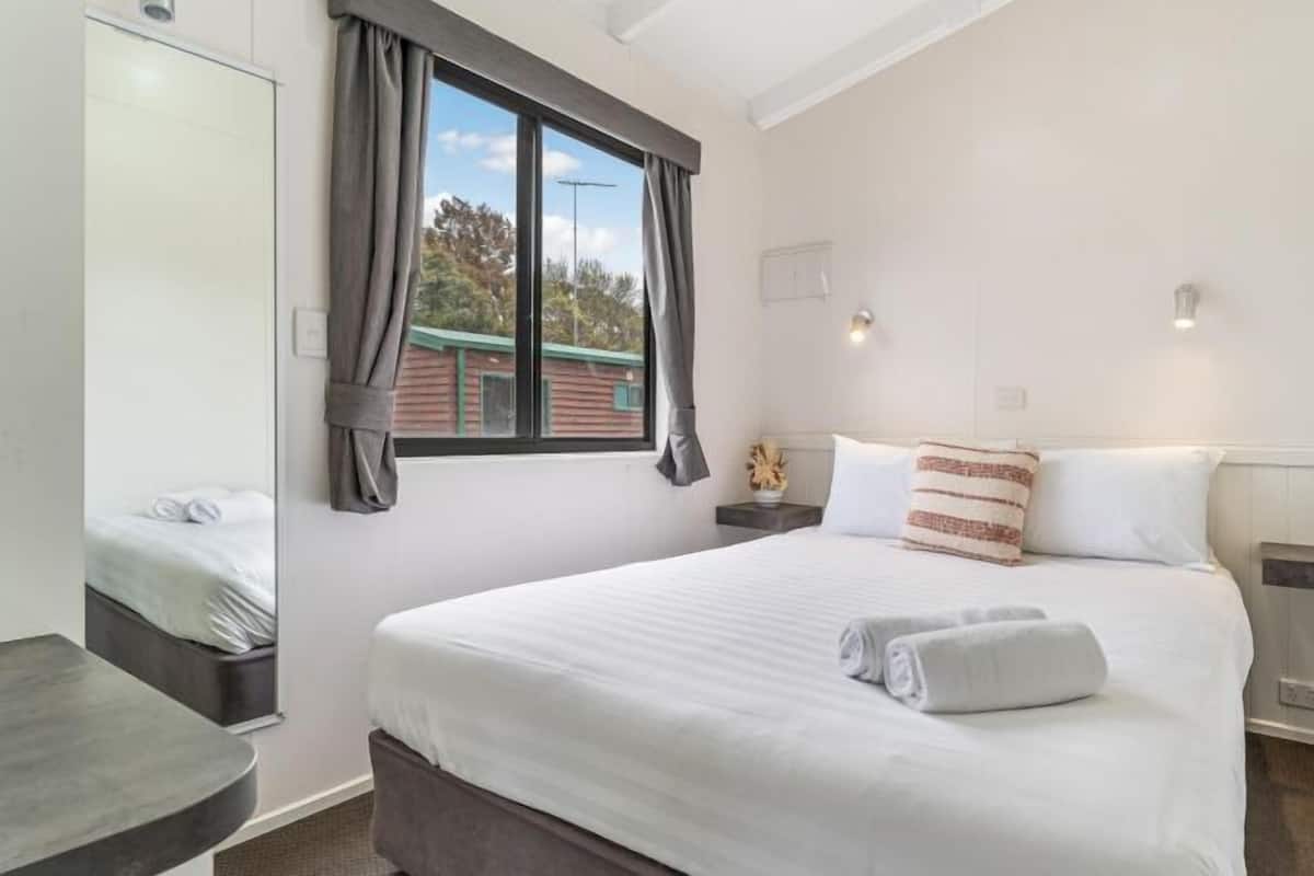 A bedroom with a large bed, a bedside table, a mirror, and a window with curtains.