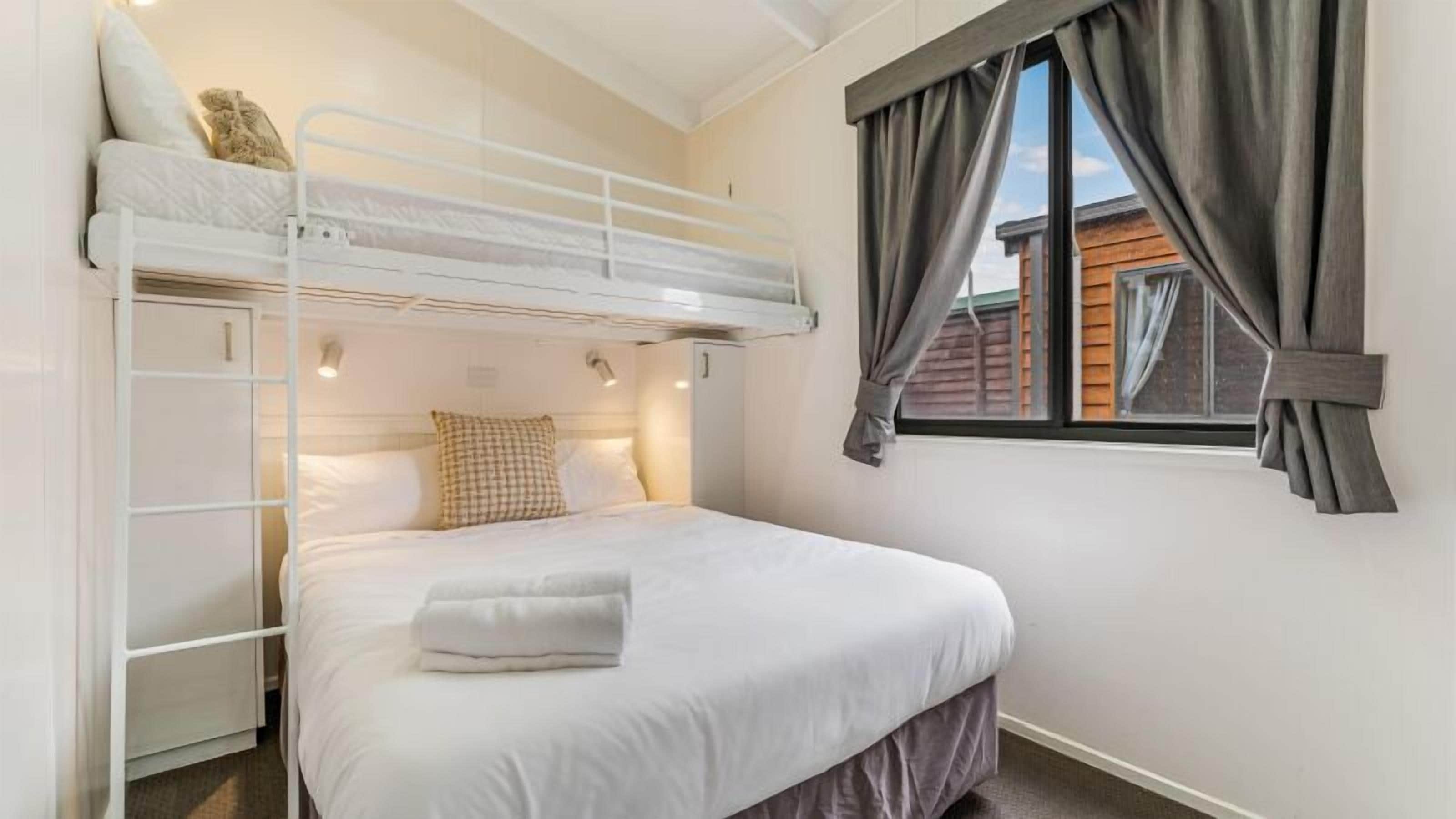 A bunk bed room with a window, curtains, and a bed with a pillow and a folded towel.