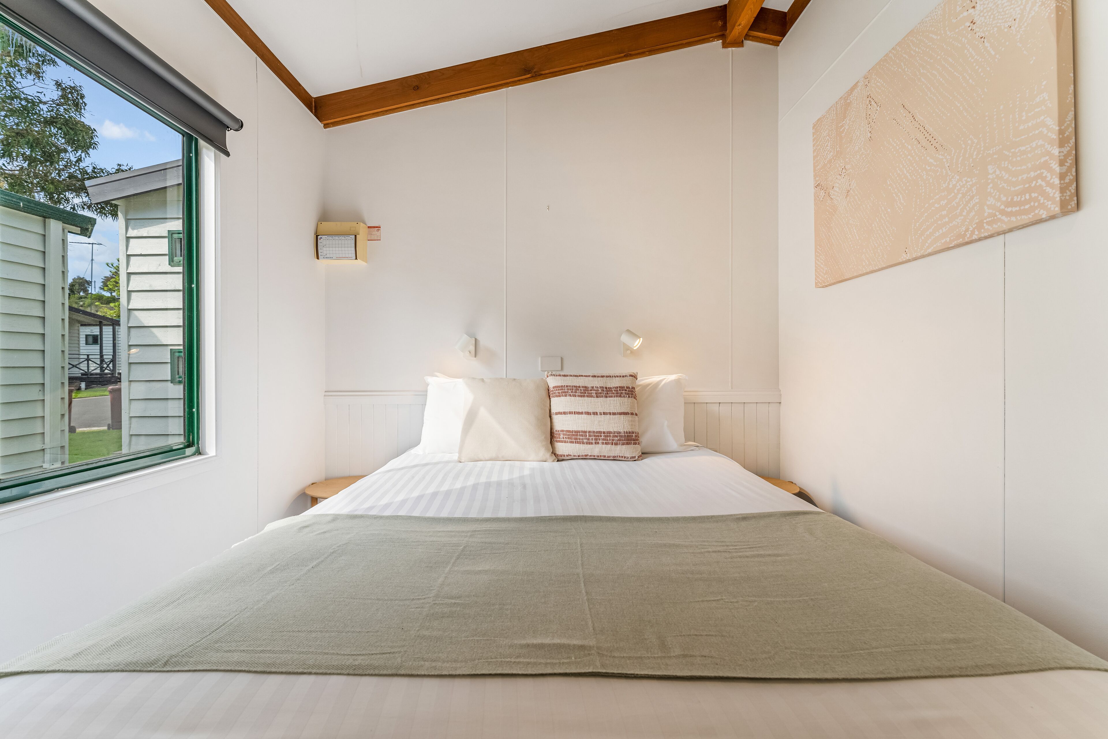 A bedroom with a large bed, a window, and a wall-mounted light fixture.