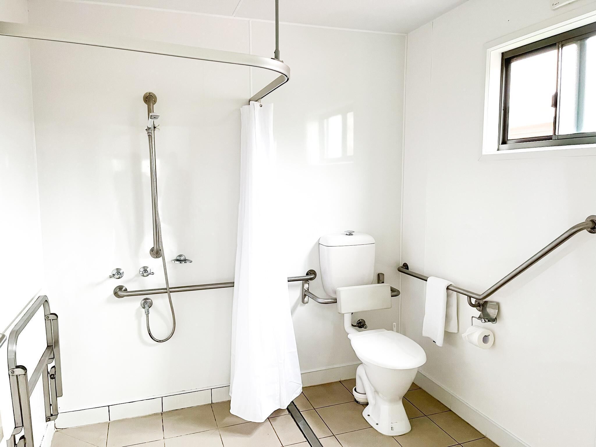 A bathroom with a shower, toilet, and grab bars.