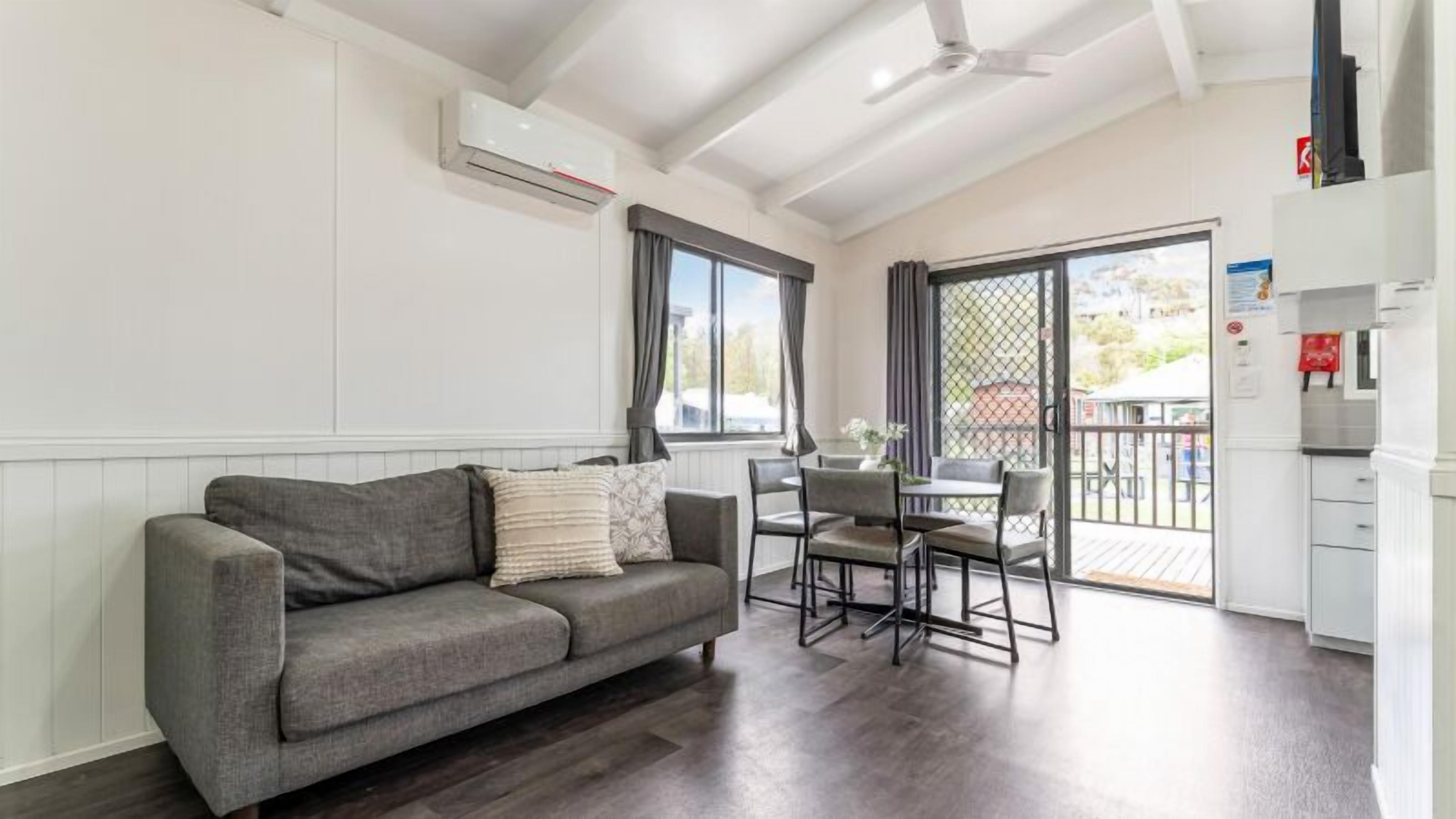 Una sala moderna con un sofá gris, una mesa de comedor con sillas y un balcón con vistas.