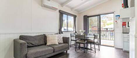 Una sala moderna con un sofá gris, una mesa de comedor con sillas y un balcón con vistas.