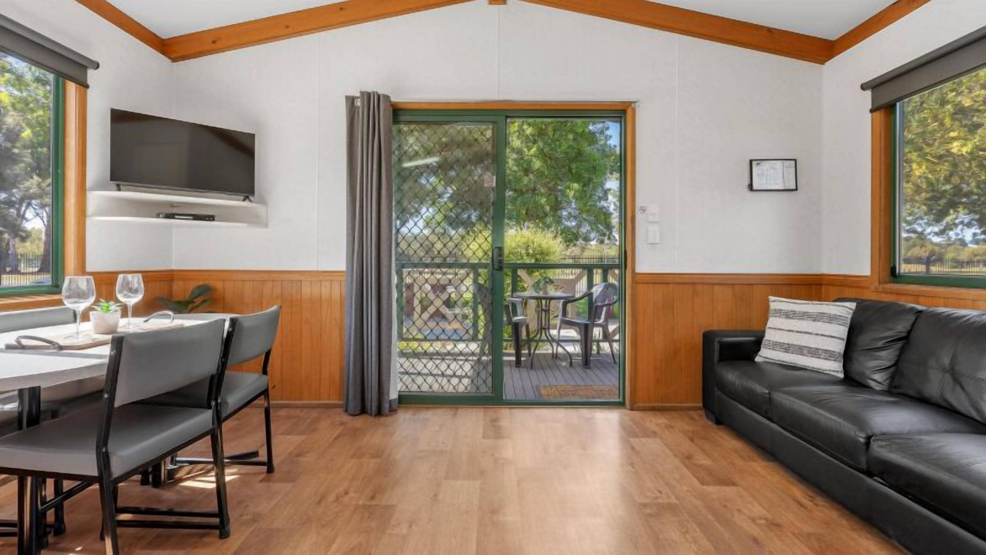 Una habitación con una mesa de comedor, sillas, un sofá de cuero negro y una puerta corredera de vidrio que da a un patio al aire libre.