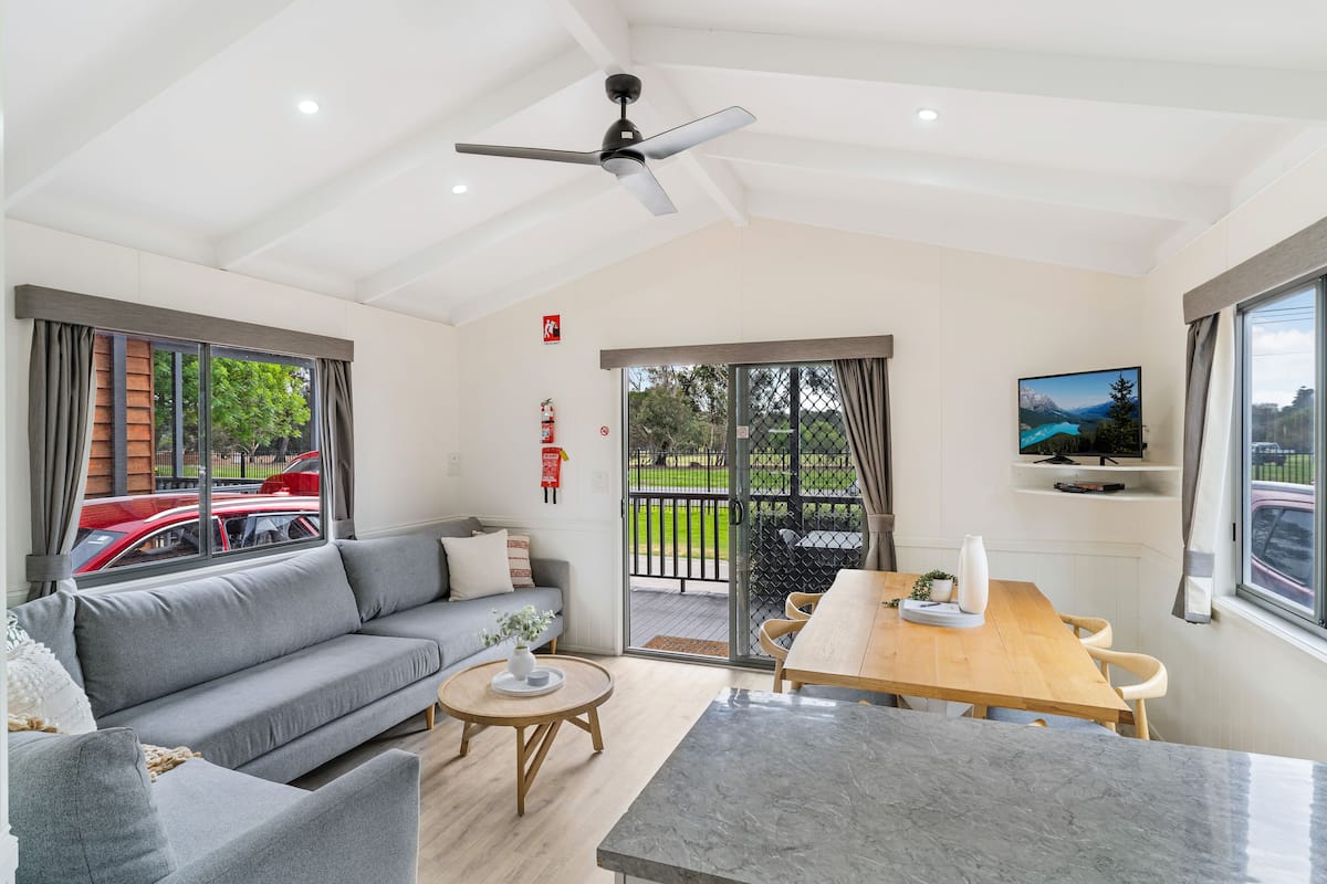 A modern living room with a grey sofa, a wooden dining table, and a ceiling fan.
