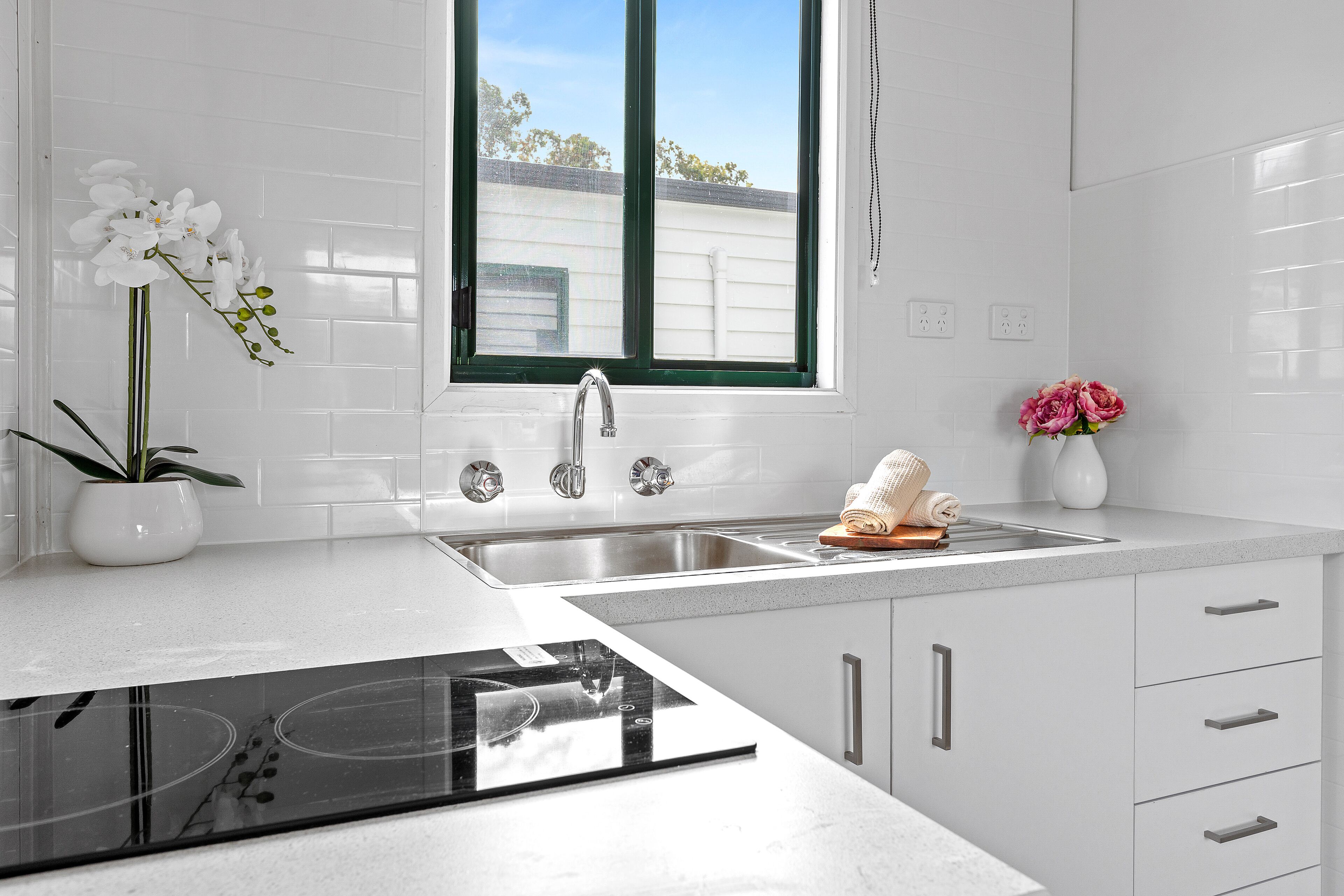A modern kitchen with a built-in stove, a double sink, and a window with a view of the outside.