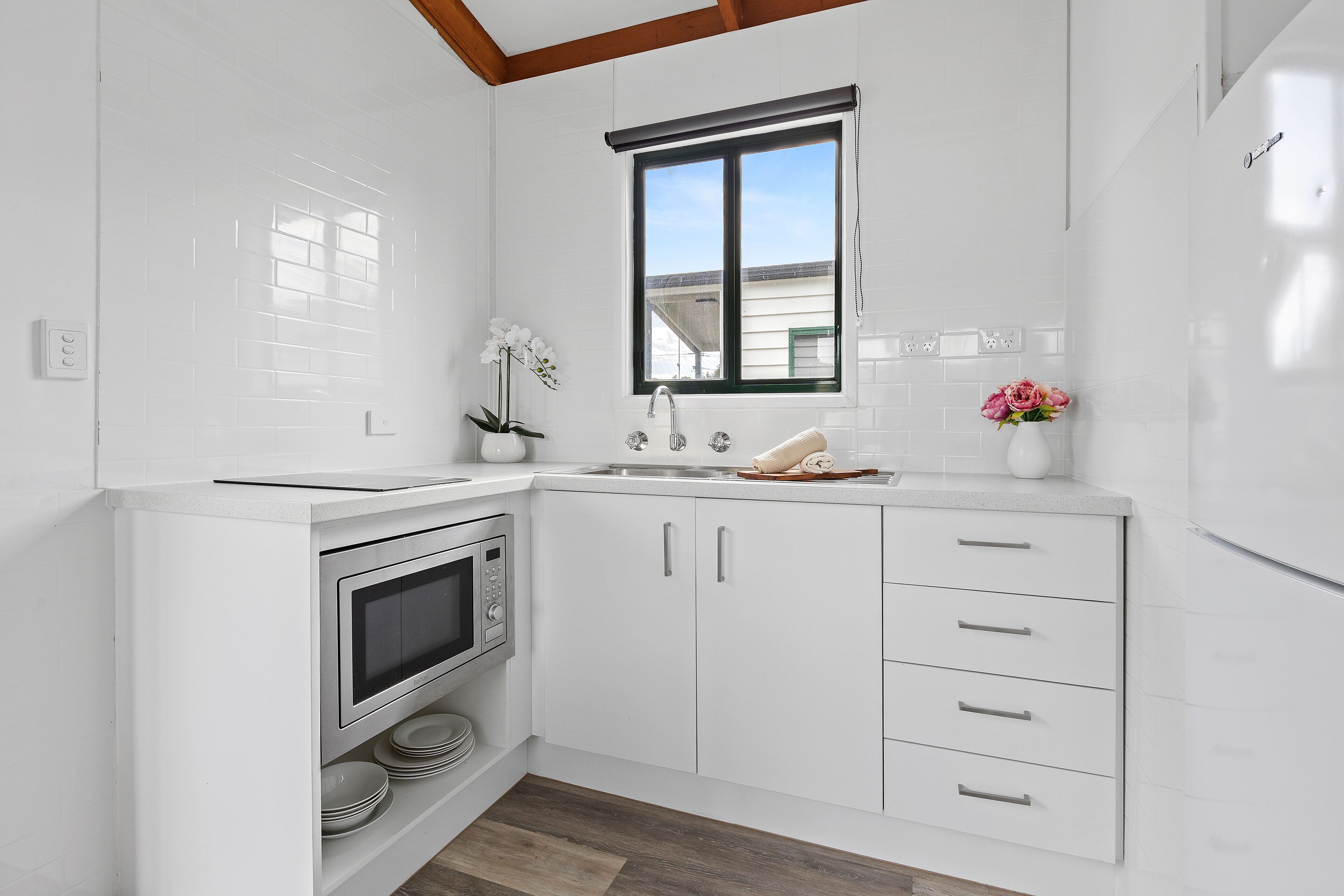 A modern kitchen with white cabinetry, a built-in microwave, and a window above the sink.