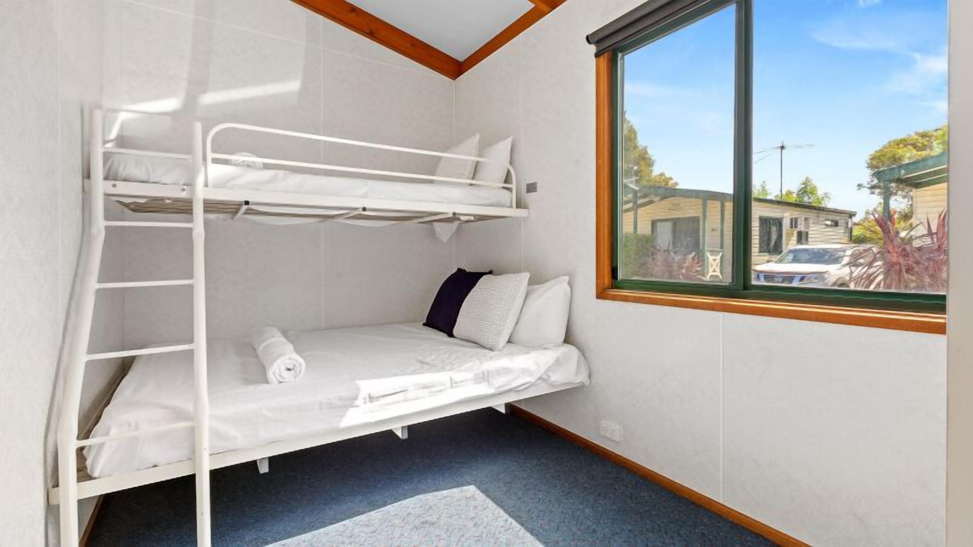 A bunk bed room with a window view of a building and parked cars.