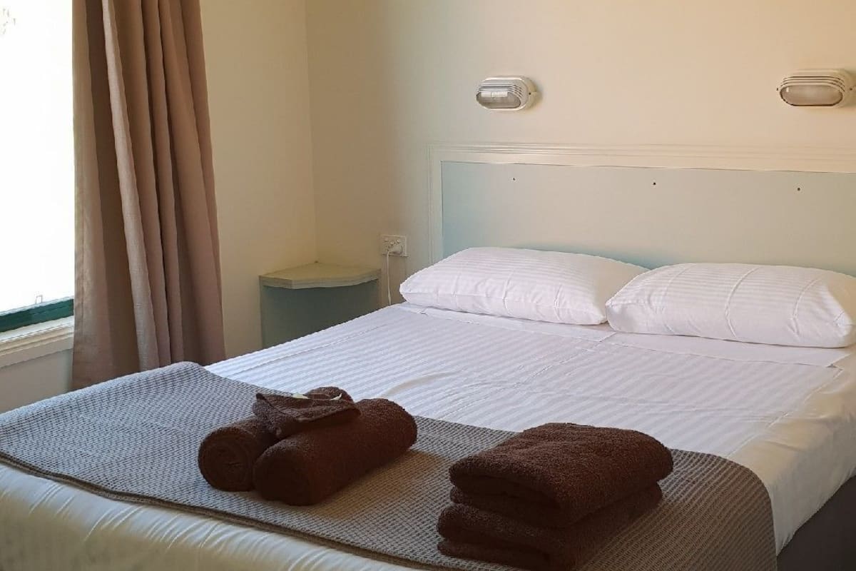 A hotel room with a bed, a nightstand, a lamp, and a window with curtains.