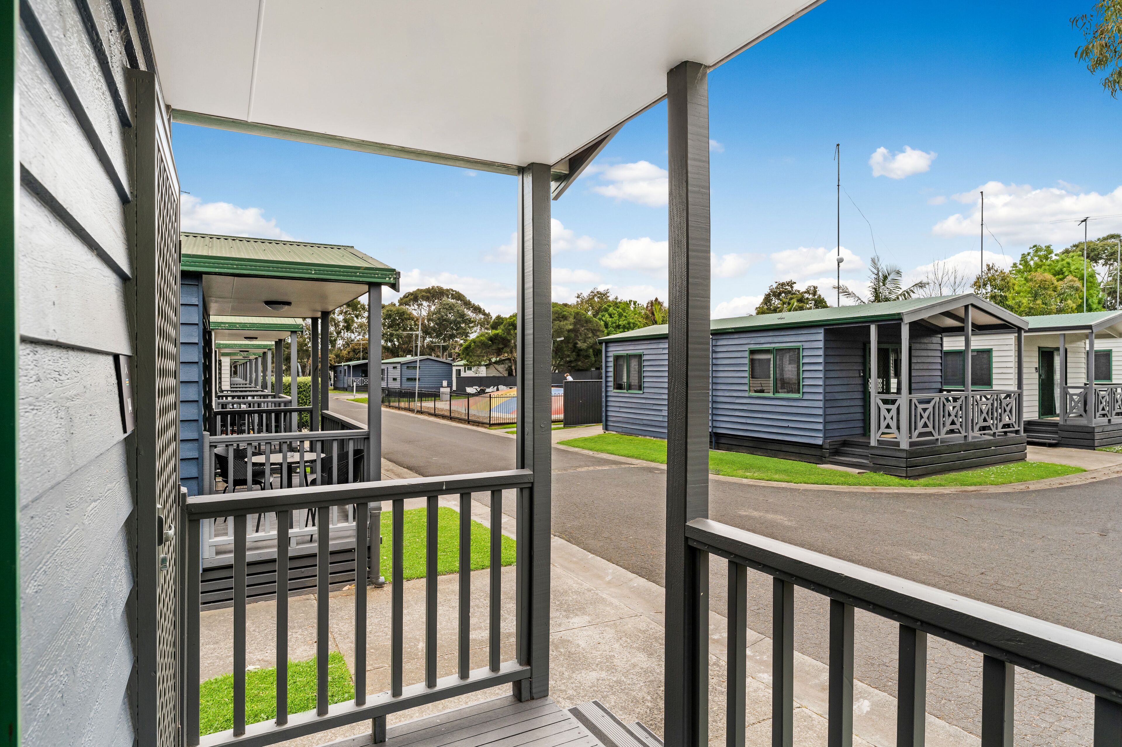 A row of mobile homes with a covered porch and a grassy lawn.