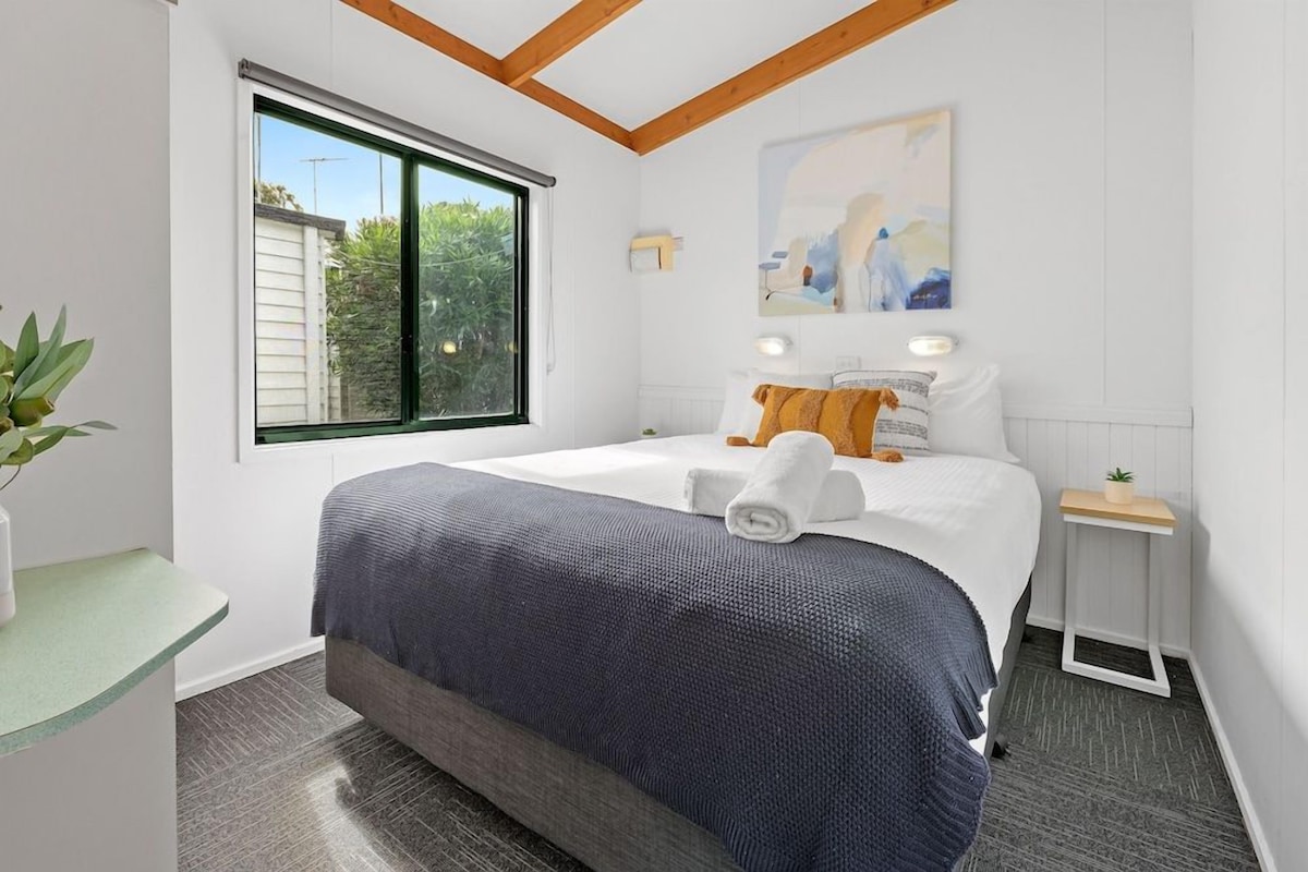 Un dormitorio con una cama grande, una ventana, una mesita de noche y un cuadro en la pared.
