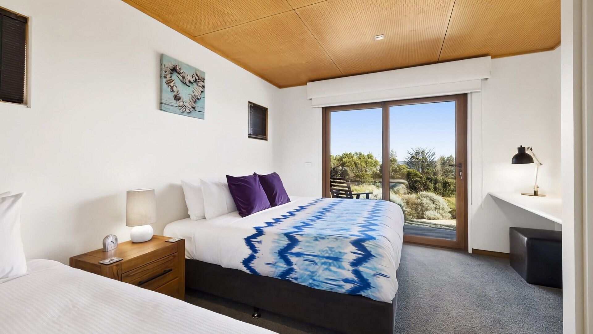 A modern bedroom with a large bed, a desk, and a view of the outdoors.
