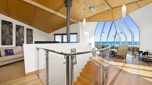 A modern interior with a wooden ceiling, a glass staircase, and a view of the ocean.