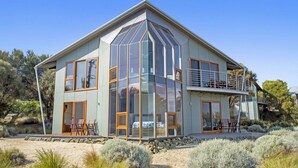 A modern two-story house with large glass windows, a balcony, and a stone foundation.