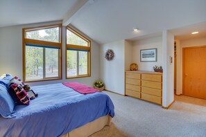 Un dormitorio con un ventanal grande, una cama con ropa de cama azul, un aparador y una puerta.