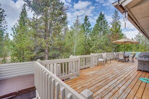 Una terraza de madera con mobiliario exterior, una parrilla y vistas a pinos.