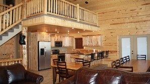 A spacious living area with a wooden staircase, a kitchen with modern appliances, and a dining area with leather seating. - Beautiful Cabin In The Trees w/Jacuzzi & Pool Table - 20 Mins From Yellowstone (Island Park)