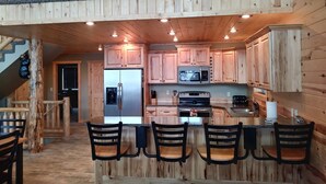 A wooden cabin interior with a kitchen featuring a refrigerator, microwave, stove, and bar area with chairs. - Beautiful Cabin In The Trees w/Jacuzzi & Pool Table - 20 Mins From Yellowstone (Island Park)