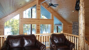 A cabin interior with wooden walls, large windows, a stone fireplace, and leather chairs. - Beautiful Cabin In The Trees w/Jacuzzi & Pool Table - 20 Mins From Yellowstone (Island Park)