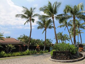 Eingang eines tropischen Resorts mit Palmen, einem Steinweg und einem Schild mit der Aufschrift 'Halili Kai'.