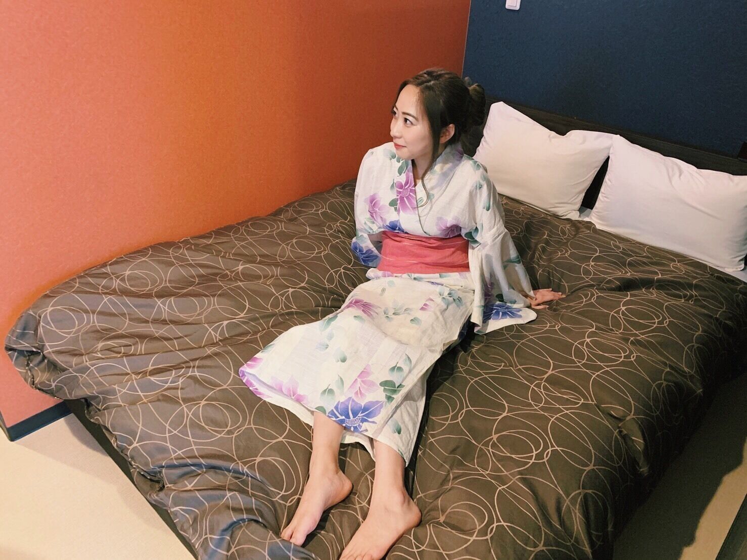 Una persona sentada en una cama con una colcha y almohadas estampadas.
