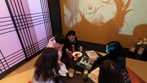 Un grupo de personas jugando un juego de mesa alrededor de una mesa redonda, con un proyector mostrando una imagen en la pared.
