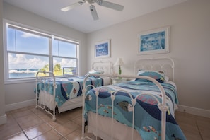 A bedroom with two beds, large windows, and a ceiling fan.