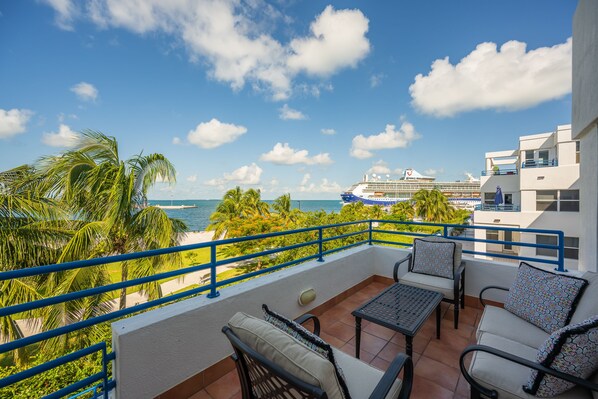 A balcony with outdoor furniture, a view of the sea, and a cruise ship in the background.