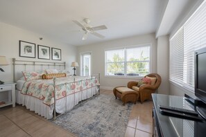 A bedroom with a bed, a chair, a TV, and a ceiling fan.