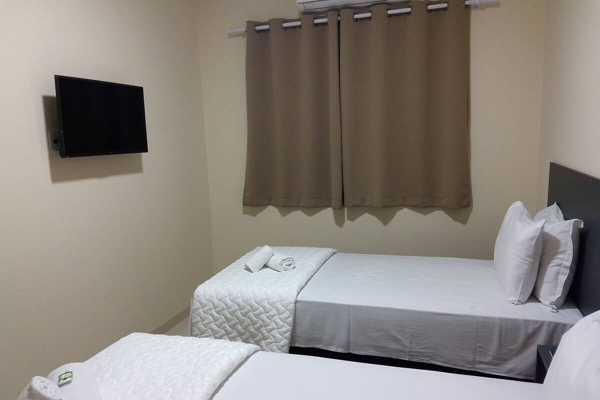 A small, clean room with two beds, a flat-screen TV, and a window with curtains.