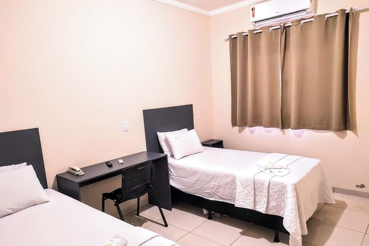A hotel room with two beds, a desk, and an air conditioning unit.