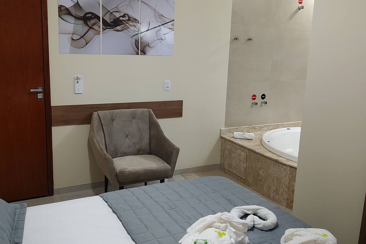 A hotel room with a bed, a chair, a large mirror, and a bathtub.