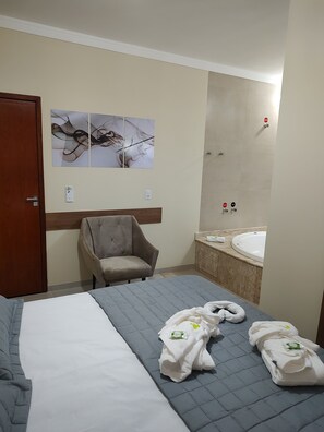 A hotel room with a bed, a chair, a large mirror, and a bathtub. - Hotel Vale Do Ivinhema (Bataypora)