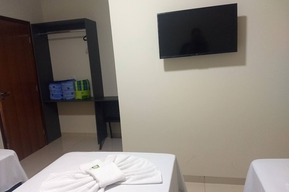 A hotel room with a bed, a TV mounted on the wall, and a mirror with shelves.