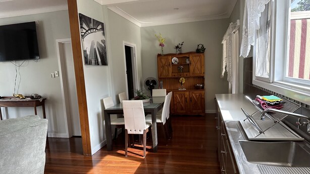 A modern kitchen with a built-in dishwasher, a dining area with a wooden table and chairs, and a large window with curtains. - Kelly's House excellent for contractors, families and pets (Bunbury)