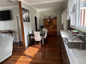 Uma cozinha moderna com máquina de lavar louça embutida, sala de jantar com mesa e cadeiras de madeira, e uma janela grande com cortinas.