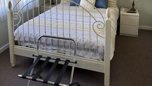 A bedroom with a metal-framed bed, a nightstand with a lamp, a ceiling fan, and a large floral artwork on the wall. - Kelly's House excellent for contractors, families and pets (Bunbury)