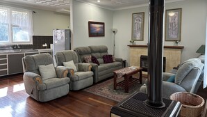 A living room with a fireplace, a sofa, a dining area, and a kitchen. - Kelly's House excellent for contractors, families and pets (Bunbury)