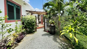A pathway leading to a house with a covered patio area, surrounded by lush greenery and a variety of plants.